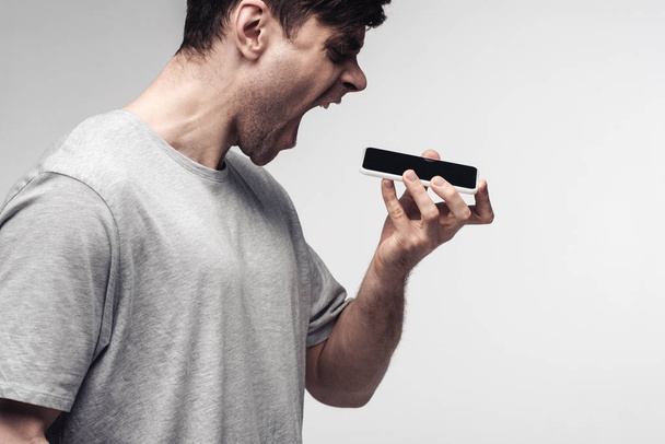 aggressive man screaming on smartphone isolated on grey - Zdjęcie, obraz