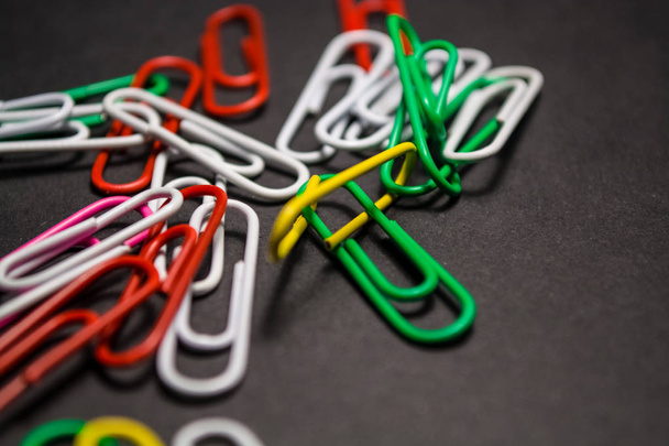 On black monophonic background plastic multi-colored paper clips   are lie. White, red, green, yellow colors. Office. - Foto, imagen