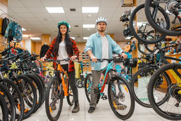 Couple in cycling helmets choosing bicycles, shopping in sport shop. Summer season extreme lifestyle, active leisure store, customers buying cycles - Photo, Image