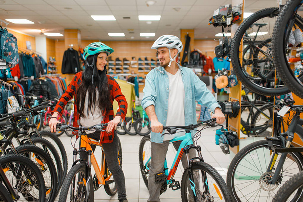 Ζευγάρι σε κράνη ποδηλασίας που επιλέγουν ποδήλατα, ψώνια στο αθλητικό κατάστημα. Θερινή σεζόν ακραία lifestyle, ενεργό κατάστημα αναψυχής, πελάτες αγοράζοντας κύκλους - Φωτογραφία, εικόνα