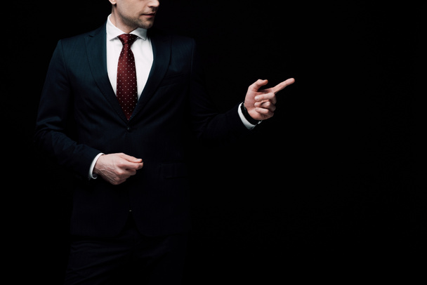 gedeeltelijke weergave van zakenman wijzend met de vinger geïsoleerd op zwart, menselijke emotie en expressie concept - Foto, afbeelding