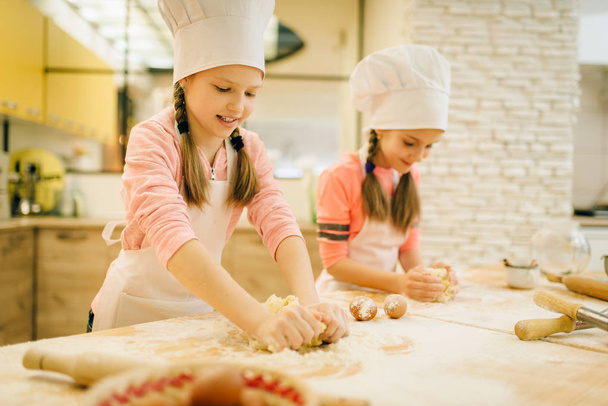 Dwie dziewczynki kucharze zgnią ciasto, ciasteczka przygotowujące do kuchni, śmieszne piekarzy. Ciasto do gotowania dla dzieci, kucharze przygotowujące placki - Zdjęcie, obraz