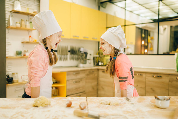 Dos chefs niñas están jugando y se divierten, preparación de galletas en la cocina. Niños cocinando pastelería, niños cocinando preparando pastel
 - Foto, Imagen
