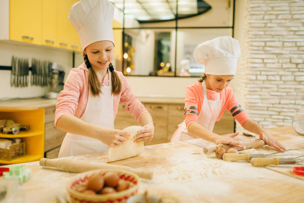 Δύο κοριτσάκια σεφ Τυλίγουμε τη ζύμη με πινέζες, τα μπισκότα προετοιμάζονται στην κουζίνα. Παιδικά μαγειρεία και διασκέδαση, τα παιδιά μαγειρεύουν προετοιμασία τούρτα - Φωτογραφία, εικόνα