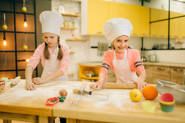 Dos chefs niñas con rodillo, preparación de galletas en la cocina, panaderos divertidos. Los niños cocinan pasteles y se divierten, los niños cocinan hacen masa y preparan pasteles
 - Foto, Imagen