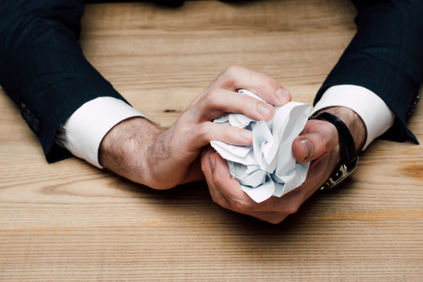 partial view of businessman sitting at table and crumpling paper  - Photo, image
