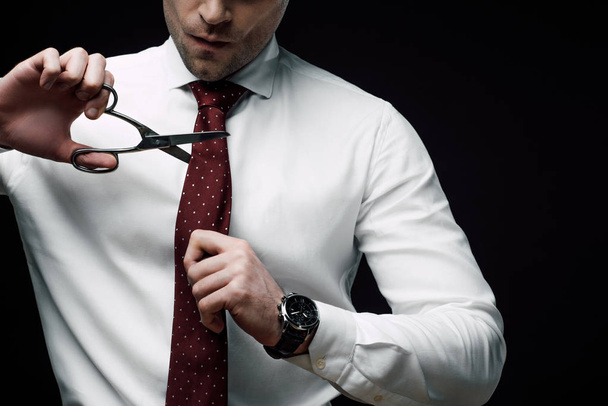 cropped view of disappointed businessman cutting tie with scissors isolated on black - Photo, Image
