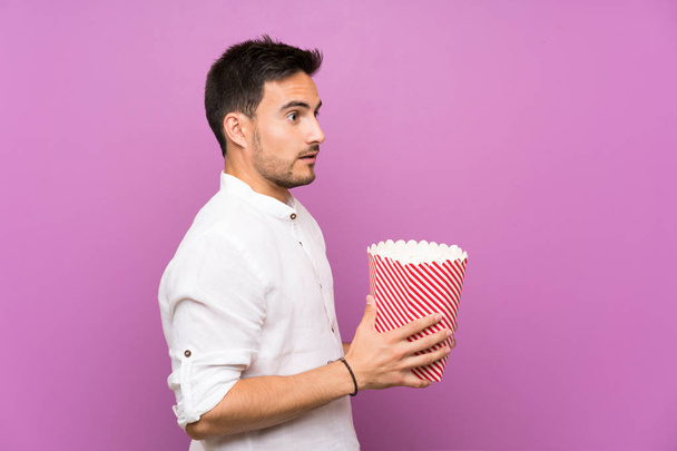 Przystojny młody człowiek na fioletowym tle trzyma popcorns - Zdjęcie, obraz