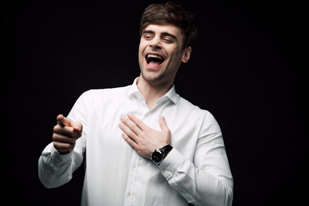 cheerful businessman laughing and pointing with finger isolated on black, human emotion and expression concept - Foto, Imagem