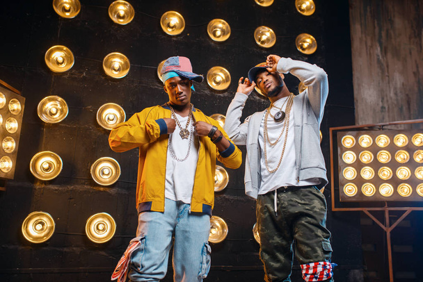 zwei afrikanische Rapper in Mützen, Künstler posieren auf der Bühne mit Scheinwerfern im Hintergrund. Rap-Performer auf der Bühne mit Licht, Underground-Musik - Foto, Bild