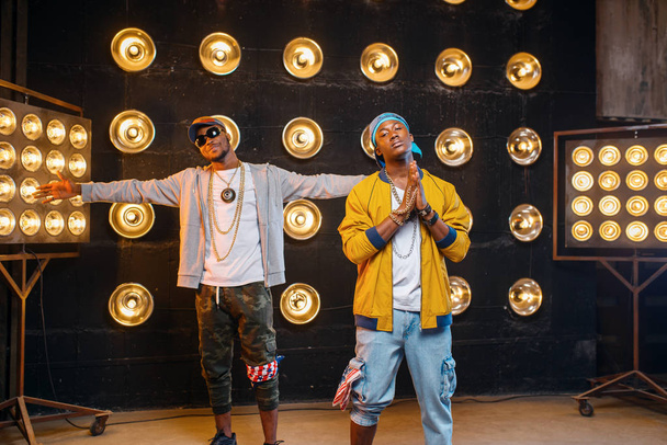 zwei afrikanische Rapper in Mützen, Künstler posieren auf der Bühne mit Scheinwerfern im Hintergrund. Rap-Performer auf der Bühne mit Licht, Underground-Musik - Foto, Bild