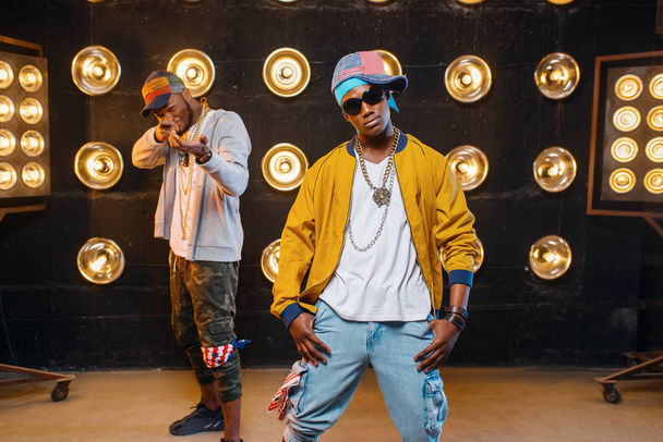 Dois rappers africanos em bonés no palco com holofotes no fundo. Artistas de rap em cena com luzes, música underground
 - Foto, Imagem
