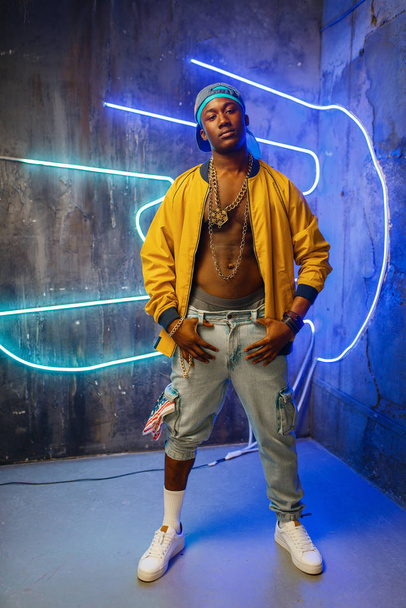 Afrikaanse rapper in onderdoorgang neon licht op achtergrond. Rap performer in Club met grunge muren, Underground Music Concert - Foto, afbeelding