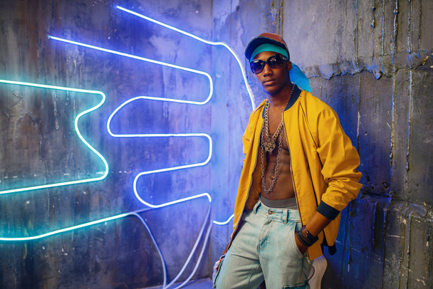 schwarzer Rapper in Unterführung mit Neonlicht im Hintergrund. Rap-Performer in Club mit Grunge-Wänden, Underground-Musik - Foto, Bild
