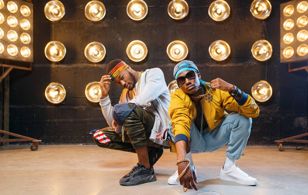Two African rappers sitting on the floor, perfomance on stage with spotlights on background. Rap performers on scene with lights, underground music, urban style - Foto, afbeelding