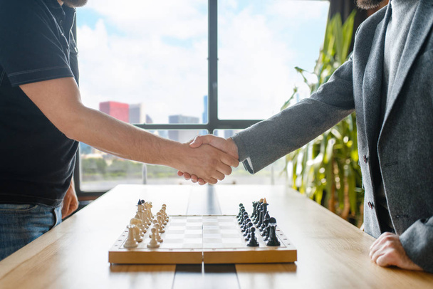 Male chess players shake hands before the game. Two chessplayers begin the intellectual tournament indoors. Chessboard on the table - Photo, Image