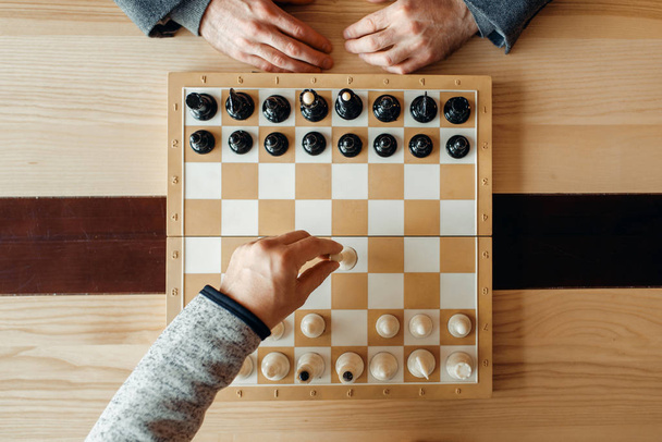 Ajedrecistas masculinos a bordo, movimiento de blanco, vista superior. Dos jugadores de ajedrez comienzan el torneo intelectual en interiores. Tablero de ajedrez sobre mesa de madera
 - Foto, Imagen