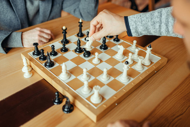 Erkek satranç oyuncuları tahtada oynarken, beyaz şövalye piyon alır. İki satranç oyuncusu entelektüel turnuvaya kapalı mekanlarda başlar. Ahşap masa üzerinde satranç tahtası - Fotoğraf, Görsel