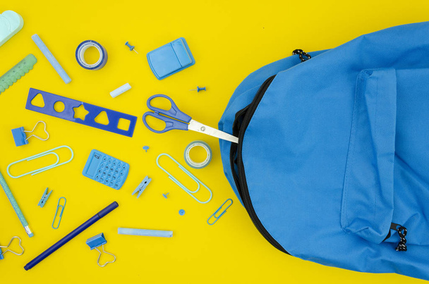 Top view blue stationery supplies with a school bag on a yellow background. Flat lay back to school concept - Zdjęcie, obraz