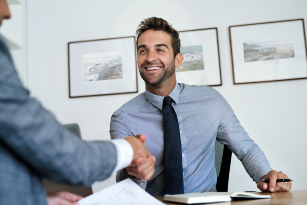 Улыбающийся менеджер сидит за своим столом в офисе и пожимает руку кандидату на работу после успешного собеседования
 - Фото, изображение