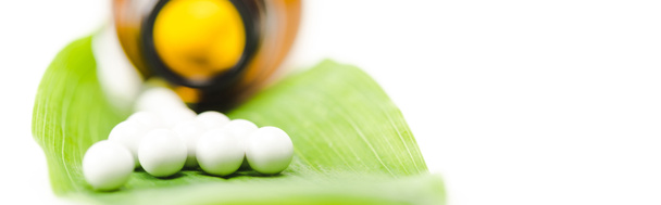 panoramic shot of small round pills on green leaf near bottle isolated on white  - Photo, Image