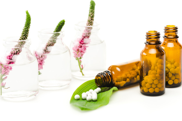 rosa verónica flores en botellas de vidrio cerca de pequeñas píldoras redondas en hoja verde sobre blanco
  - Foto, Imagen