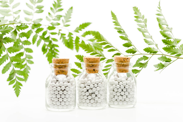 selective focus of small pills in glass bottles with wooden corks near green leaves on white  - Foto, afbeelding