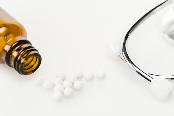 selective focus of round small pills near stethoscope and glass bottle on white  - Foto, imagen
