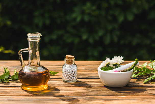 glass bottle with pills near flowers in mortar near pestle on wooden table  - Photo, Image