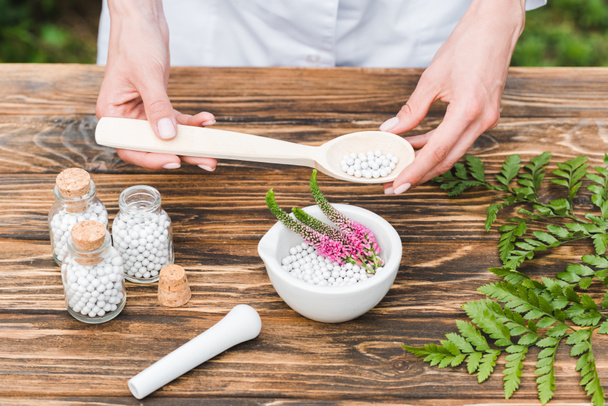 top view of woman holding spoon with pills near mortar with veronica flowers and green leaves on wooden table  - Photo, Image