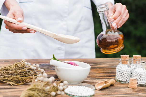 enfoque selectivo de la mujer sosteniendo cuchara y jarra con aceite cerca de mortero con flores de verónica en la mesa de madera
  - Foto, Imagen