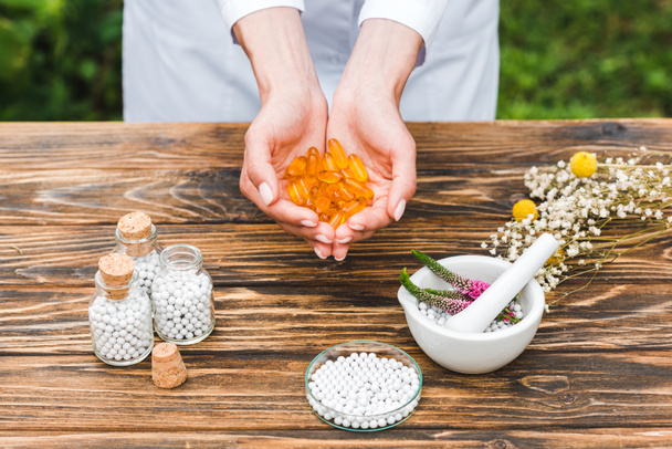 cropped view of woman holding pills near bottles and mortar with veronica flowers on wooden table  - Photo, Image