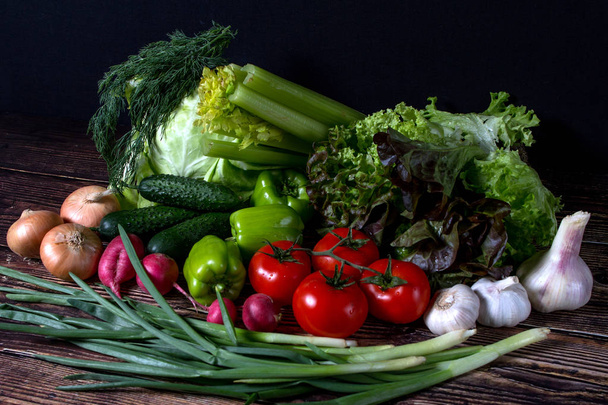 set of fresh vegetables in the dark. vegetarian food on wooden background. vegetable harvest from the garden. - 写真・画像