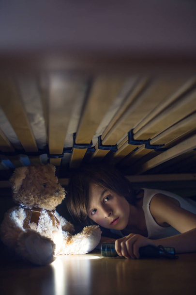 Little child, hiding under the bed, hugging teddy bear and holdi - Foto, afbeelding
