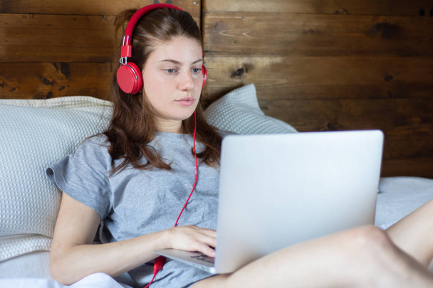 Young woman using laptop and headphones in bed. - Foto, Imagen
