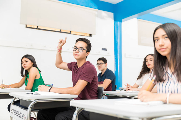 Confident student with raised hand attending lecture in classroom at school - Photo, Image