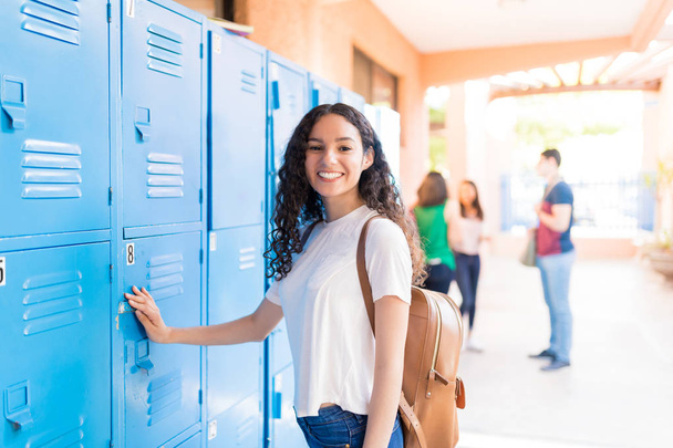 Porträt eines lächelnden Teenagers, der an Schließfächern in der Universität steht - Foto, Bild