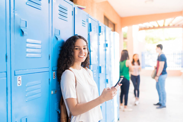 Sorridente adolescente caucasico utilizzando smartphone nel corridoio della scuola superiore
 - Foto, immagini