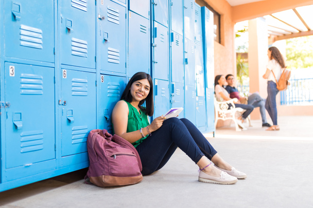 Retrato de menina atraente estudando enquanto sentado por mochila no corredor da escola
 - Foto, Imagem