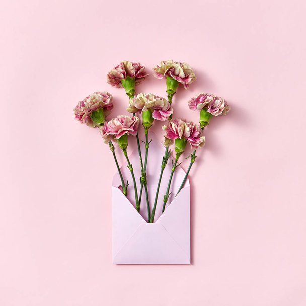 Handmade blank envelope with bouquet of carnations flowers on a pastel pink background, copy space. Top view. Greeting card - Фото, зображення