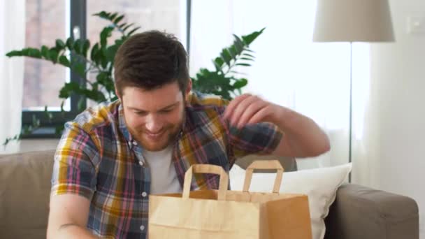 man unpacking and eating takeaway food at home - Filmati, video