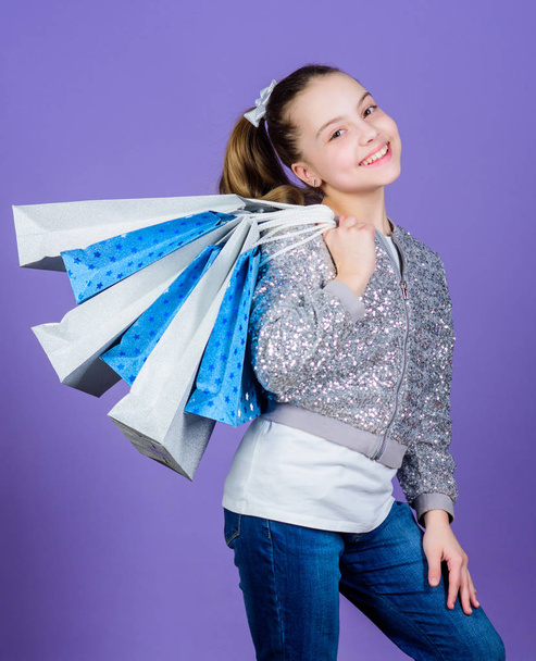 Black friday. Sale discount. Shopping day. Child hold bunch packages. Kids fashion. Birthday girl. Favorite brands and hottest trends. Girl with shopping bags violet background. Shopping and purchase - Foto, afbeelding