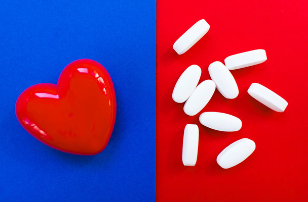 rotes Herz mit Pillen auf rotem und blauem Hintergrund.. Konzept der Herzkrankheit - Foto, Bild