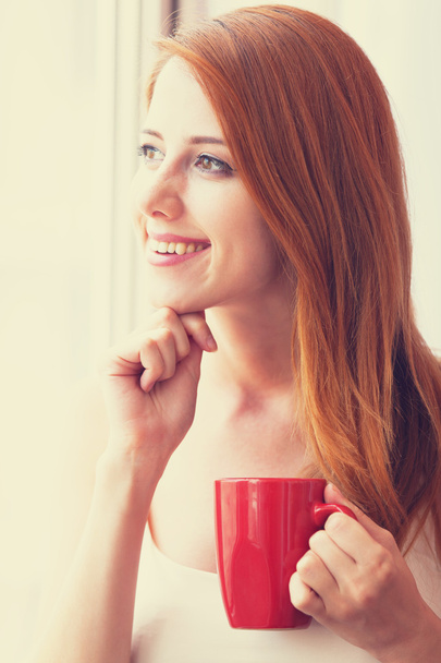 Beautiful young woman with cup over window. - Photo, Image