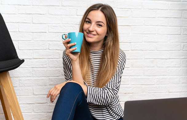 Fiatal nő ül a padlón vele laptop kezében egy csésze o - Fotó, kép