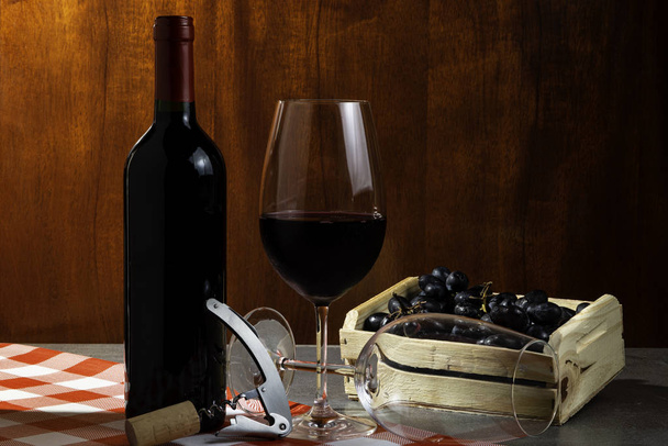 Butelka czerwonego wina w piwnicy z winem do degustacji. Czerwone drewniane tło z drewnianym pudełku z winogronem. Koncepcja tradycji i kultury wina. - Zdjęcie, obraz