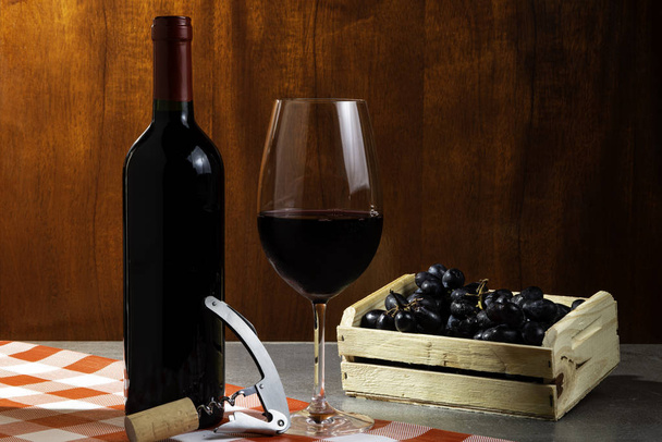 Botella de vino tinto en bodega para degustación. Fondo rojo de madera con caja de madera con uvas. Concepto de tradición y cultura del vino
. - Foto, Imagen
