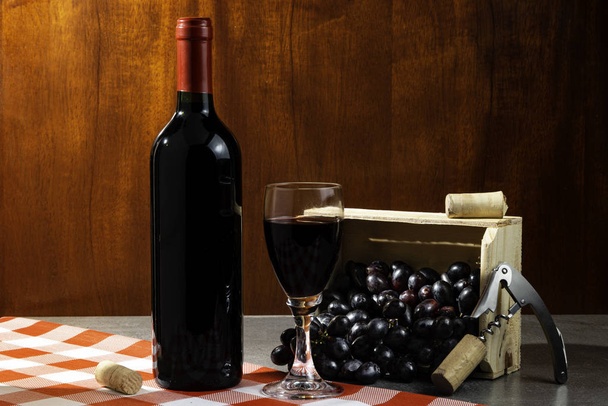 Pullo punaviiniä viinikellarissa maisteluun. Punainen puinen tausta puinen laatikko viinirypäleitä. Viini perinne ja kulttuuri käsite
. - Valokuva, kuva