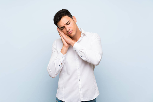 Handsome man over blue wall making sleep gesture in dorable expression - Фото, изображение