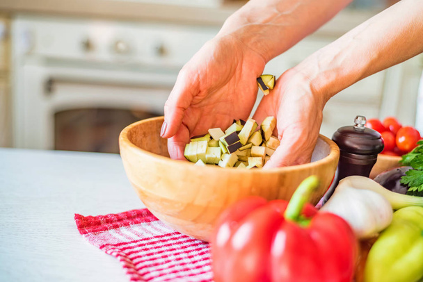 weibliche Hand legte geschnittene Auberginen in Holzschüssel in der Küche. Gemüse kochen - Foto, Bild